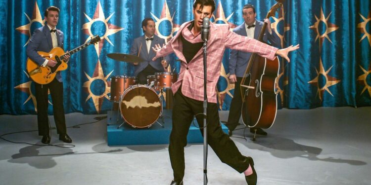Austin Butler as Elvis, performing on stage with a band behind him, in ELVIS