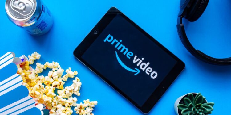 Prime Video logo appears on a tablet surrounded by a can of soda, spilled popcorn, headphones and a cactus