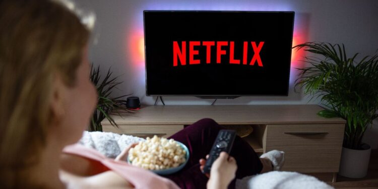 Woman with popcorn bowl holding remote to watch Netflix on television