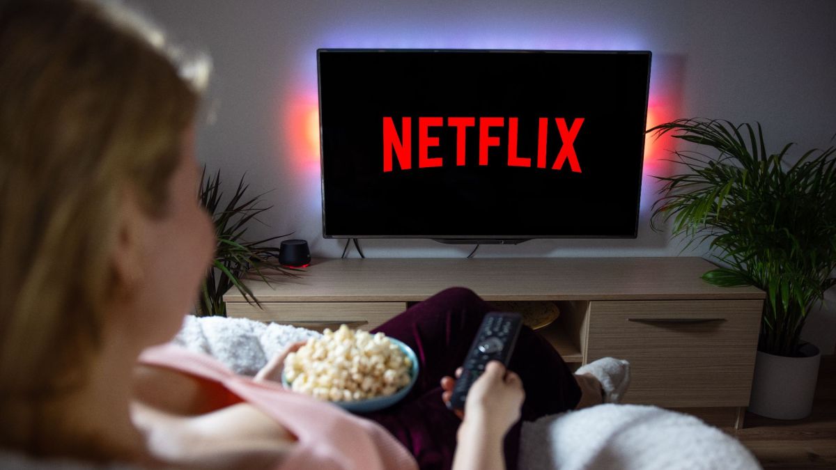 Woman with popcorn bowl holding remote to watch Netflix on television